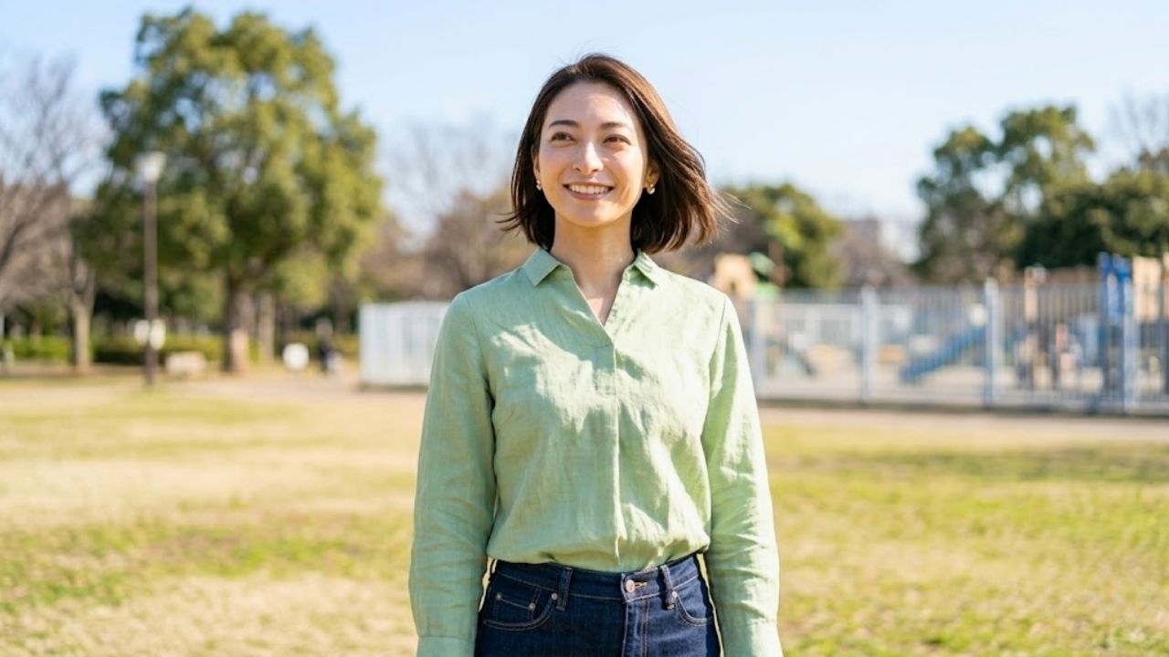 明るく開けた公園で、少し離れた場所から前を見つめ、ホッとしたような、限りなく優しく幸せそうな母の笑顔を浮かべる20代のシングルマザー。慎重なステップを経て、いよいよ子どもと彼を屋外で引き合わせている安心感を表現している。