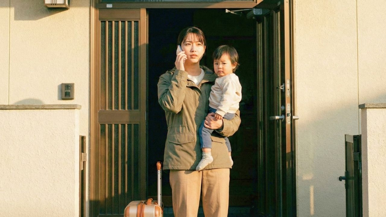 決意に満ちた表情で、幼い子どもを抱きながら家の玄関前で電話をかける若い母親。足元にはスーツケースがあり、モラハラ環境から抜け出し、新しい生活に向けてSOSの行動を起こした瞬間を捉えている。