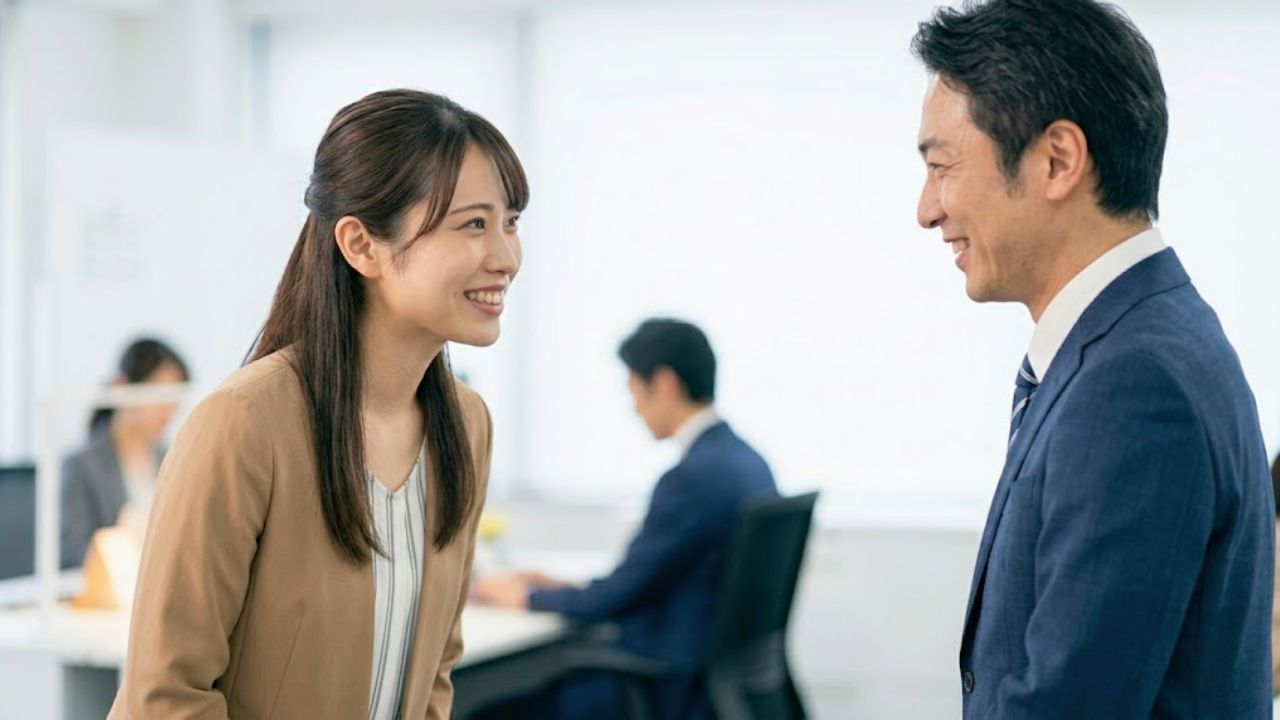 会社の飲み会を断った翌朝、明るいオフィスで上司に爽やかで誠実な笑顔で挨拶とフォローのコミュニケーションをし、良好な関係を保つシングルマザー